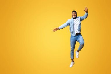 Neşeli bin yıllık siyah adam eğleniyor, sarı arka planda havaya zıplıyor, boş yer var.