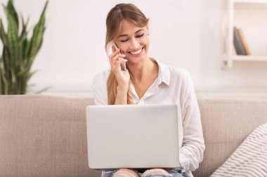 Telefondan konuşan mutlu kadın laptopta çalışıyor, koltukta oturuyor. Modern Yaşam Tarzı ve Serbest Kariyer. Seçici Odaklanma