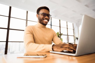 Ortak çalışma kavramı. Modern ortak iş yerinde dizüstü bilgisayarda çalışan mutlu bir Afrikalı serbest yazar. Boşluğu kopyala