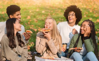 Sarışın kız, çok ırklı arkadaşlarıyla piknik yapıyor, dışarıda lezzetli pizzaların tadını çıkarıyor.