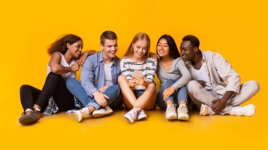 Gençlerin yaşam tarzı. Çok ırklı bir grup genç yerde oturuyor ve akıllı telefon ekranlarına, panoramasına bakıyor.
