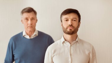 Ciddi Olgun Adam ve kıdemli babası beyaz arka planda duran kameraya bakıyor. Panorama, Seçici Odaklanma