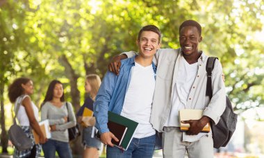 Two international students smiling guys posing at camera at public park, having break while studying