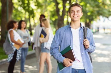 Attractive young guy student spending time with friends together after university, public park