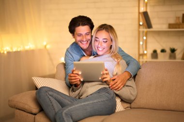 Mutlu genç çift tablet kullanıyor ve sıcak kış akşamında birlikte vakit geçiriyorlar.