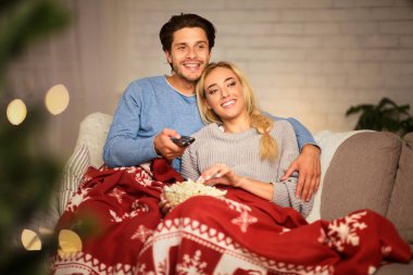 Noel arifesinde aşık bir çift patlamış mısırın tadını çıkarıyor ve evde televizyon seyrediyor.