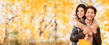 Mutlu aşık kız, neşeli erkeğine arkadan sarılıyor, sonbahar ormanında poz veriyor, boşluğu kopyalıyor.