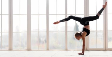 Genç, sportif, esnek bir kadın yoga yapıyor. Amuda kalkmış bacaklarla poz veriyor. Kapalı alanda, yoga stüdyosunda, boş alanda.