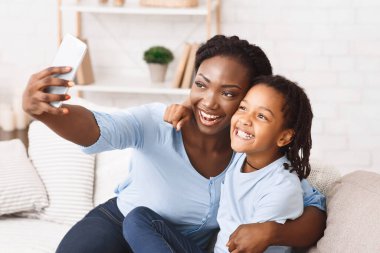 Capturing Happy Moments. African mother and daughter sitting on the couch and taking selfie in the living room