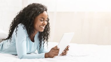 İlginç bir içerik. Milenyum Afrikalı kız dijital tablet hakkında blog okuyor, yatakta yatıyor, boş yer var.