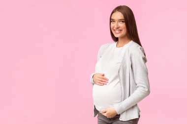 Hamilelik Mutluluğu. Neşeli Bekleyen Kadın Dokunaklı Göbek Pozisyonu Beyaz Stüdyo Arkaplanındaki Kameraya Bakıyor. Metin için Boşluk