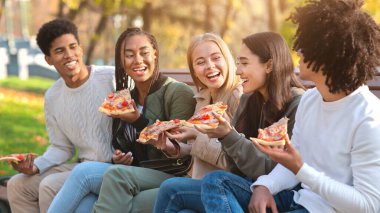 Aç gülen uluslararası gençler parkta vakit geçirirken pizzanın tadını çıkarıyorlar.