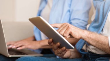 Modern büyükanne ve büyükbaba. Gadget'lar kullanarak kıdemli çift, tablette internette sörf adam, dizüstü bilgisayarda kadın, closeup