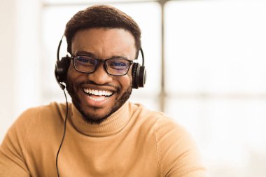 Yardım hattı konsepti. Ofiste kameraya bakarken, kulaklık takmış gülümseyen bir zenci resmi. Boş boşluk