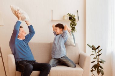 Dedem ve ninemle yatıya kaldım. Mutlu çocuk ve büyükbabası yastıklarla kavga ediyor. Evdeki koltukta oturup eğleniyorlar.