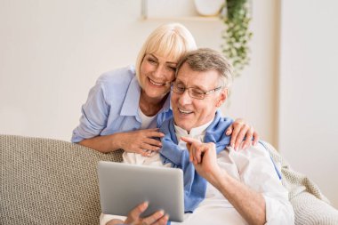 Tablet kullanan, haber okuyan ve evde kanepede dinlenen mutlu yaşlı çift