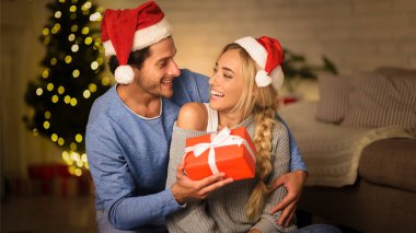 Christmas gift. Happy couple celebrating Christmas at home, man giving present to wife