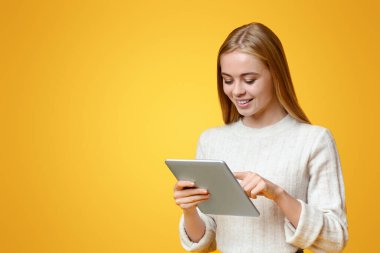 Öğrenciler için uygulama. Portakal rengi stüdyo arka planında dijital tablet kullanan güzel bir genç kız, kopya alanı olan bir panorama.