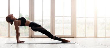 Yoga stüdyosunun penceresinden yukarıya doğru bakan esnek bir kızın yan görüntüsü.