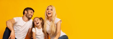 Mutlu bir aile birlikte vakit geçirmekten zevk alır, kahkahalar ve gülümsemeler paylaşır. Ebeveynler ve kızları yerde rahatça oturuyorlar, sıcaklık ve neşe saçıyorlar, boşluğu kopyalıyorlar.