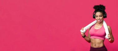 Spor salonu, fitness konsepti. Kırmızı arka planda havlusu ve kulaklığı olan gülümseyen siyah kız, kopya alanı olan panorama.