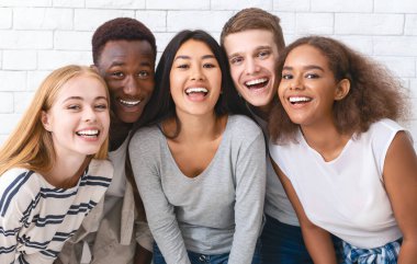 Portrait of happy multiethnic young friends students having fun over white wall background, close up