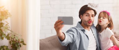 Babası ve güzel kızı evde selfie çekiyor, taç takıyor ve ruj sürüyor, ördek suratları yapıyor.