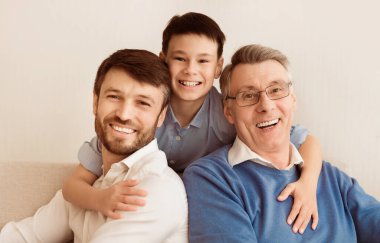 Erkek Nesli. Mutlu çocuk, baba ve büyükbabaya sarılıyor. Kameraya gülümsüyor. Evdeki koltukta birlikte oturuyorlar..