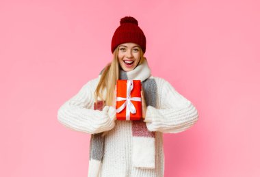 Kırmızı şapkalı mutlu kız elinde Noel hediyesi, sarı stüdyo arka planı, fotokopi alanı