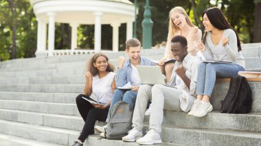 Bir grup uluslararası öğrenci başarıyı kutluyor, sınav sonuçlarını internetten kontrol ediyor, parkta vakit geçiriyor.