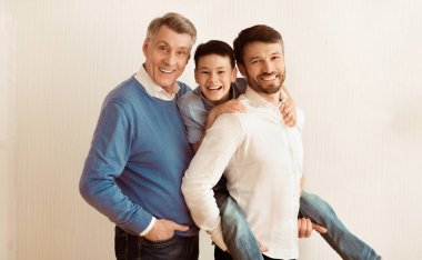 Erkek Aile Kavramı. Pozitif Çocuk, Baba ve Büyükbaba kameraya bakıyor Beyaz Duvar 'a bakıyor.