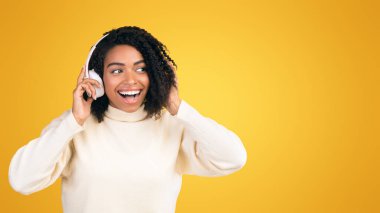 Popüler Müzik Dinliyorum. Sarı stüdyo duvarında izole edilmiş kulaklıklara dokunan heyecanlı siyah kız.