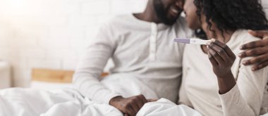 Mutlu siyah çift hamilelik testi pozitif sonuç veriyor. Evde sarılıp öpüşüyorlar. Yakın plan.