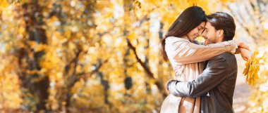 Romantik çift, sonbahar ormanında flört ederken sarılıyor. Kopya alanı olan bir panorama.