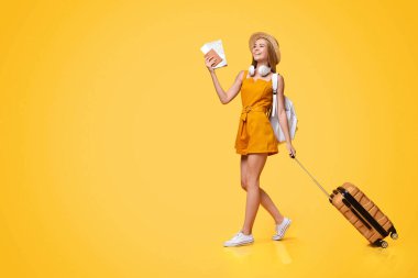 Karantina sonrası seyahatler. Biletlerle yürüyen neşeli genç kız ve sarı stüdyonun arka planında çanta, panorama