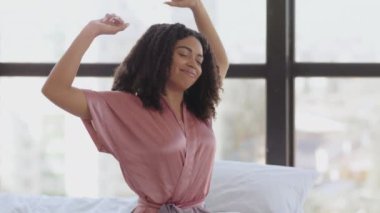 Tembel bir sabah. Genç güzel uyuyan Afro-Amerikan kadın pijamalarını giyiyor, yatakta oturuyor, uyanıyor, yeni günü selamlıyor.