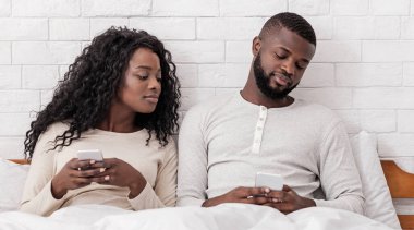 Kıskançlık ve aldatma kavramı. Evdeki biriyle mesajlaşırken kocasının cep telefonuna gizlice bakan meraklı siyah kadın.