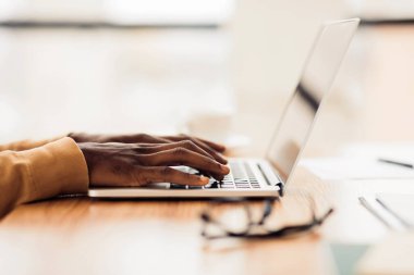 Teknoloji Konsepti. Yan görünüş ve ahşap ofis masaüstüne dizüstü bilgisayarda yazı yazan afro adamın ellerini kapat.