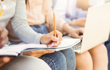 Cropped of girl student taking notes, studying with friends, using notepad and pencil