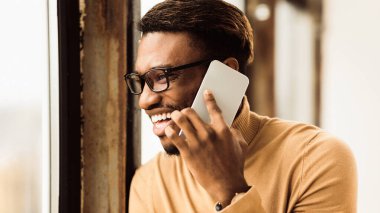 İletişim Konsepti. Zenci işadamı cep telefonuyla konuşuyor, pencereden dışarı bakıyor. Kopyalama alanı olan Panorama