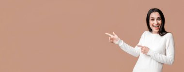 Güzel teklif. Neşeli esmer kız sarı arkaplanı işaret ediyor, iki eliyle bir şey öneriyor, içi boş bir panorama.