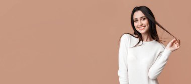 Gülümseyen esmer kız sarı arka planda uzun güzel saçlarına dokunuyor, kameraya bakan oyuncu kadın, boş alan.