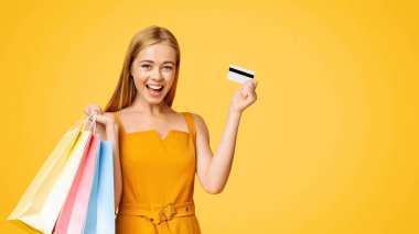 Satış ve İndirim. Alışveriş torbaları ve kredi kartı ile heyecanlı genç kızın portresi sarı arka planda duruyor, boş yer var.