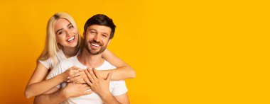 Neşeli bir çift birbirlerine sarılırken geniş bir gülümseme sergiliyor, sevgilerini ve mutluluklarını gösteriyor. Parlak sarı arka plan anın sıcaklığını arttırır, boşluğu kopyala