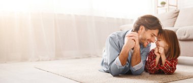 Yakışıklı baba ve liitle kızı yerde yatıyorlar ve birbirlerine bağlanıyorlar, birlikte mutlular, evin içi, boş yer.