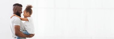 Siyah baba, genç kızına sevgiyle sarılıyor ve birlikte keyifli bir anı paylaşıyorlar. Atmosfer parlak ve neşeli, bağlarını yansıtıyor, kopyalama alanı.