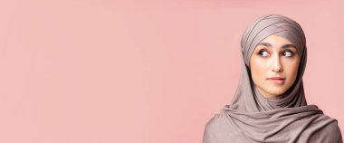 Kafiyeli, dudak ısıran, pembe arkaplandaki kopya boşluğuna bakan, şüpheli Müslüman kızın yakın plan portresi.