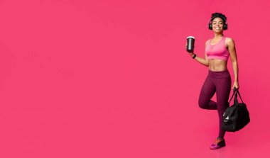 Heyecanlı kulaklıklı Afrikalı fitness kızı, spor salonuna gidiyor, kırmızı arka plan.