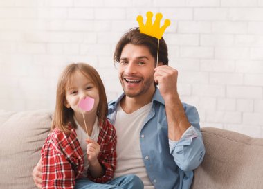 Baba ve kızı kameraya poz veriyor. Taçları ve dudakları var. Evin içi, fotokopi alanı.