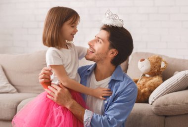 Küçük güzel kız babasının kafasına tacı takıyor, evde birlikte oynuyorlar, boş yer var.